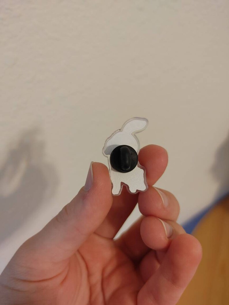 May include: White enamel pin of a rabbit with a black pin back.