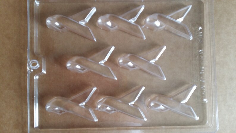 May include: A clear plastic mold with six airplane-shaped cavities. The mold is designed for making chocolate or candy airplanes.