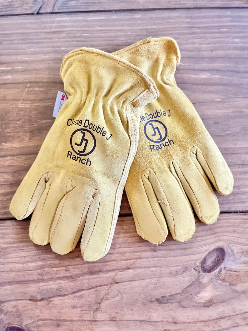 May include: A pair of tan leather work gloves with the text "Circle Double J Ranch" and a logo of a stylized "J" in a circle on each glove.