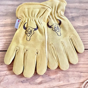 May include: A pair of tan leather work gloves with a brown bull skull logo and the text "3M Scotchgard" on the wrist.