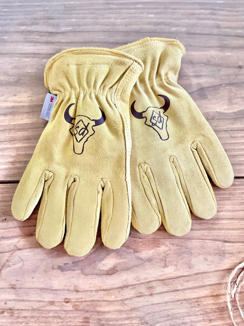 May include: A pair of tan leather work gloves with a brown bull skull logo and the text "3M Scotchgard" on the wrist.