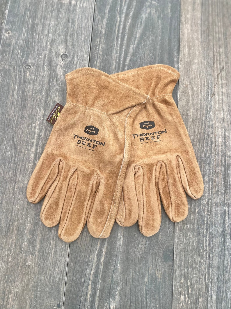 May include: A pair of brown leather work gloves with the text "Thornton Beef" on each glove.