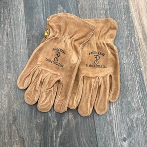 May include: A pair of brown leather work gloves with the text "PAGE CREST LAND & CATTLE LLC" and a logo of a "P" with a circle around it.