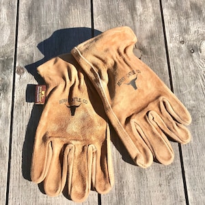 May include: A pair of brown leather work gloves with the text "Berry Cattle Co." and a bull's head logo on each glove.