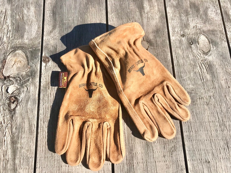 May include: A pair of brown leather work gloves with the text "Berry Cattle Co." and a bull's head logo on each glove.