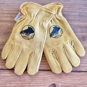 May include: A pair of tan leather work gloves with a black logo that says "Circle G Angus" on each glove.