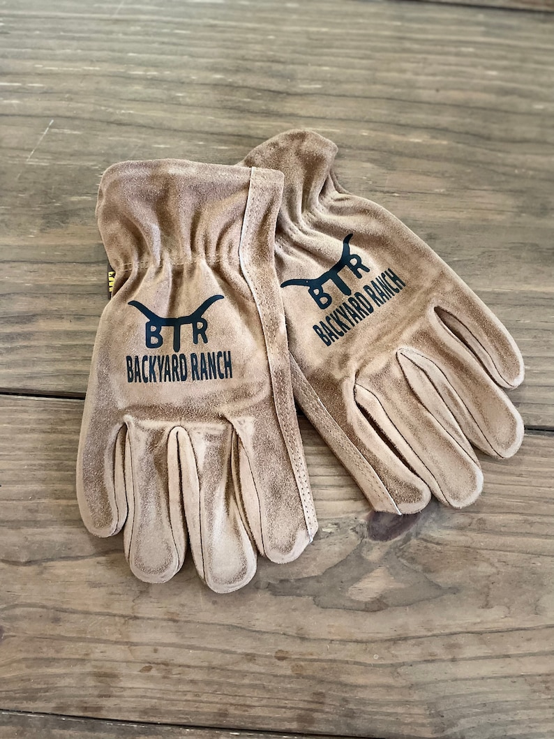 May include: A pair of brown leather work gloves with black stitching and the text "BTR BACKYARD RANCH" on each glove.