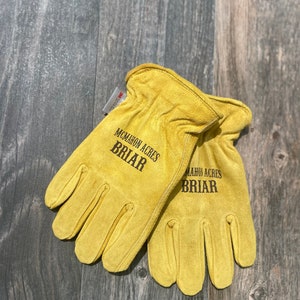 May include: A pair of yellow leather work gloves with the text "McMahon Acres Briar" printed on them.