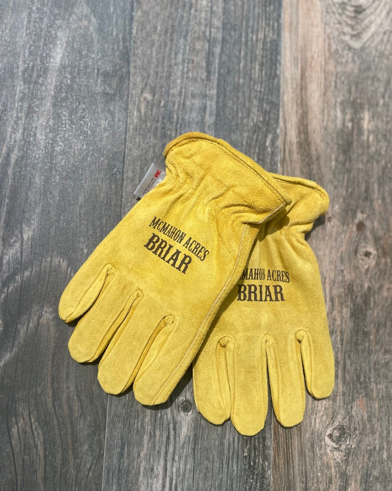 May include: A pair of yellow leather work gloves with the text "McMahon Acres Briar" printed on them.