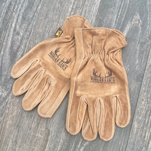 May include: A pair of brown leather work gloves with the text "Morgan Ranch" embroidered on each glove. The gloves have a white stitching detail around the wrist.