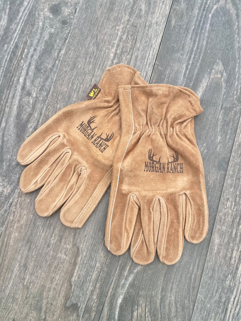 May include: A pair of brown leather work gloves with the text "Morgan Ranch" embroidered on each glove. The gloves have a white stitching detail around the wrist.