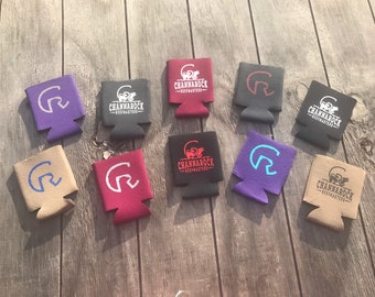 May include: Assortment of ten colorful can coolers with a white logo that says "Channarock Beefmasters" and a white stylized letter "R" with a curved line above it. The coolers are in various colors including black, red, purple, tan, and blue.