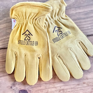 May include: A pair of tan leather work gloves with the logo "2S Steele Cattle Co" on each glove.