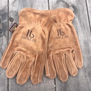 May include: A pair of brown leather work gloves with the logo "Cattle Co" embroidered on each glove.