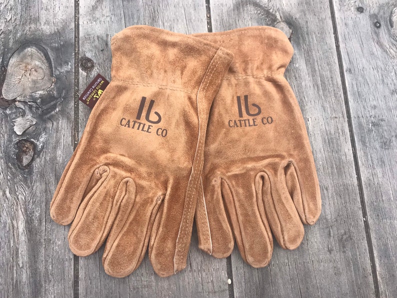 May include: A pair of brown leather work gloves with the logo "Cattle Co" embroidered on each glove.