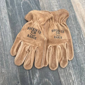 May include: A pair of brown leather work gloves with the text "Rockin' CB Ranch" on each glove.