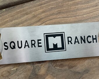 May include: A silver bottle opener with a black engraved logo that says "SQUARE M RANCH".