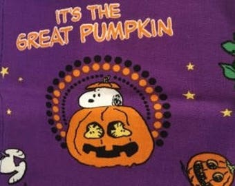 May include: Purple fabric with a repeating pattern of a pumpkin with a jack-o'-lantern face, stars, and a Peanuts character, Snoopy, dressed as a ghost, sitting on top of the pumpkin. The text "It's the Great Pumpkin" is printed in white on the fabric.