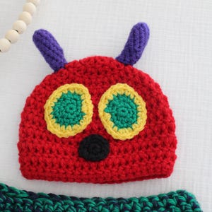 Peut inclure: Un chapeau rouge en crochet avec des antennes violettes, des yeux verts et jaunes et un nez noir. Le chapeau est conçu pour ressembler à la chenille du livre pour enfants La chenille qui fait des trous.
