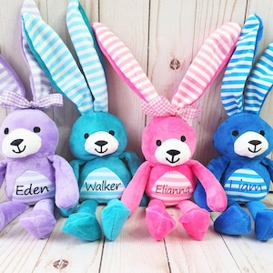 May include: Four plush bunny toys with striped ears and bows. The bunnies are purple, teal, pink, and blue. Each bunny has a name embroidered on its chest: Eden, Walker, Elianna, and Liam.