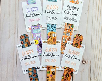 May include: Six Halloween-themed slap bracelets with different designs and personalized messages. The bracelets feature orange, black, and white colors with images of pumpkins, ghosts, bats, and candy corn. The messages on the bracelets include "Slappy Halloween" and "Love Jack".