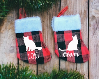 May include: Two red and black buffalo check Christmas stockings with white cat silhouettes and the names "Loki" and "Oliver" written below.