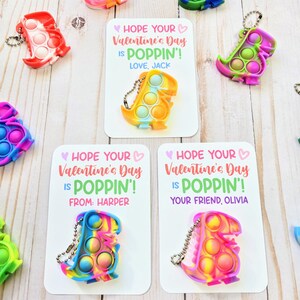 May include: Three Valentine's Day cards with colorful dinosaur-shaped pop-it fidget toys attached. The cards have the text "Hope your Valentine's Day is Poppin'!". One card says "Love, Jack", another says "From: Harper", and the third says "Your friend, Olivia".