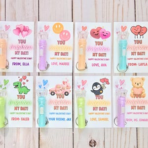 Op de afbeelding: Een verzameling Valentijnskaarten met kleine zaklampen eraan. Elke kaart bevat de zin "You Brighten My Day!" en een Valentijnsdagboodschap. De kaarten hebben verschillende ontwerpen, waaronder harten, smiley's en stripfiguren.