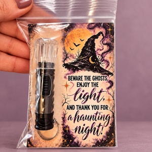 May include: A black plastic flashlight keychain with a clear faceted top, packaged in a clear plastic bag with a decorative card featuring a witch hat, a full moon, bats, and the text: BEWARE THE GHOSTS, ENJOY THE light, AND THANK YOU FOR a haunting night!