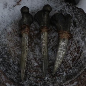 May include: Three dark, weathered bone tools with rounded heads and pointed tips. Each bone is wrapped with brown twine near the top and features white, hand-carved runic symbols etched along the length of the shaft, creating a textured appearance.