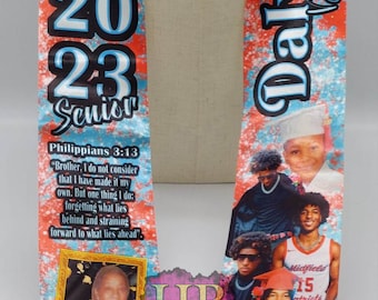May include: A graduation stole with a blue, red, and white design. The stole features the text "Class of 2023 Senior" and "Dalvin Dawson." It includes photos and the text "Midfield High School" and a Bible verse.