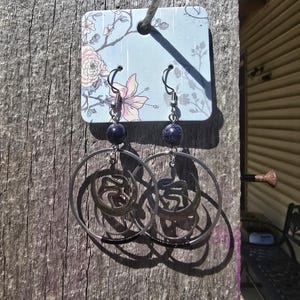 Puede incluir: Un par de pendientes de aro de plata con una cuenta de piedra azul en cada pendiente. Los pendientes cuelgan de una tarjeta con estampado floral.