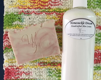 May include: A white bottle of Honeysuckle Dream Handcrafted Aloe Lotion with a pink and white bar of soap on a colorful knitted fabric.