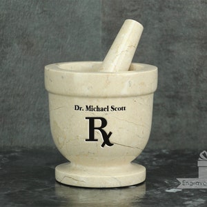 May include: A beige marble mortar and pestle set. The mortar has a wide bowl and a small base. The pestle is cylindrical. The text "Dr. Michael Scott" and the Rx symbol are printed on the mortar.