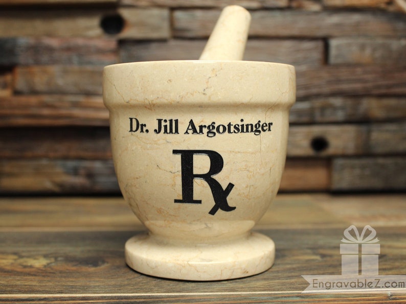 May include: A beige mortar and pestle set with the text "Dr. Jill Argotsinger" and a black Rx symbol. The pestle rests inside the mortar. The mortar is on a wooden surface.