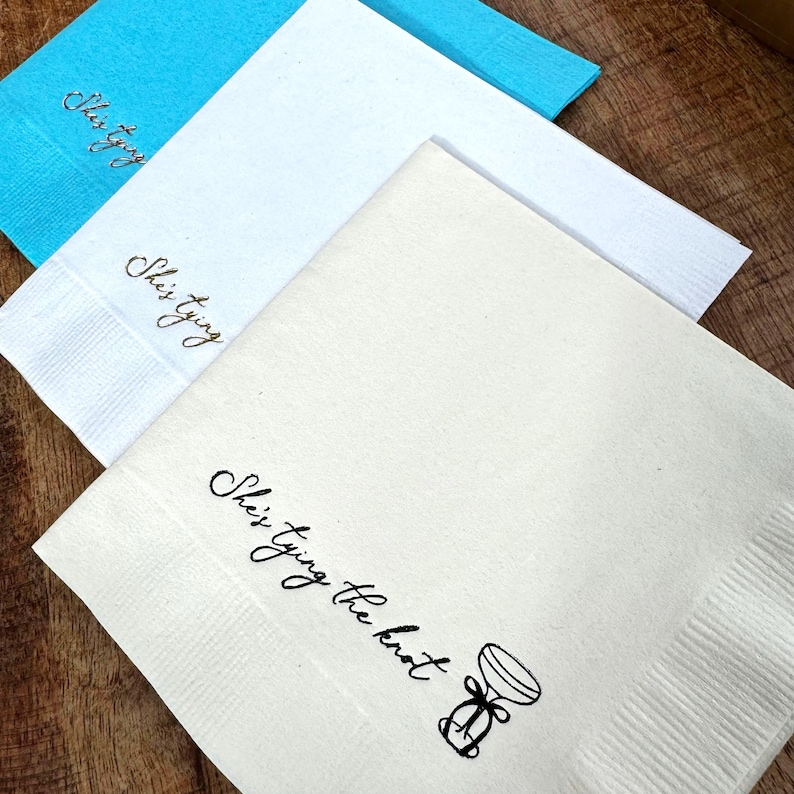 Bridal Shower Cocktail napkins that read She's tying the knot with an espresso martini coup glass with a bow.  The napkins are stamped in black and gold foil.