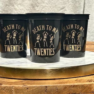 black 16 ounce stadium cups that read Death to my Twenties with 3 dancing skeletons in a gold metallic ink.  30th Birthday Cups black and gold