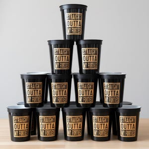A pyramid of black plastic cups with gold lettering that reads "STRAIGHT OUTTA MY FORTIES". 50th Birthday Table Decorations