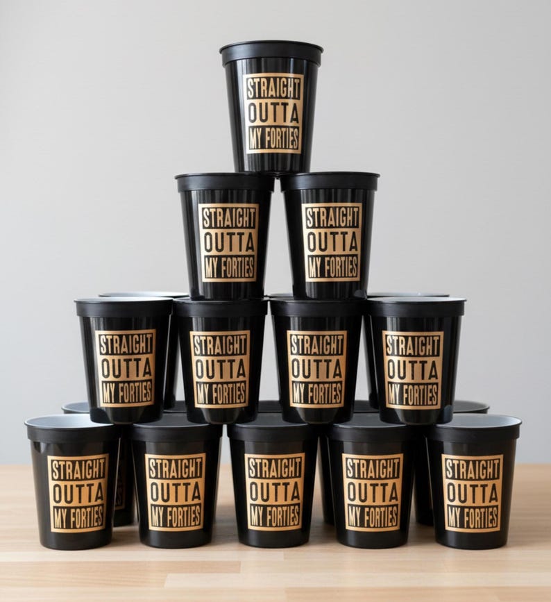 A pyramid of black plastic cups with gold lettering that reads "STRAIGHT OUTTA MY FORTIES". 50th Birthday Table Decorations