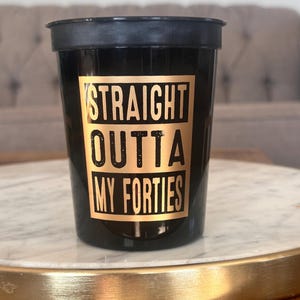 A single black cup featuring a gold box and text that reads Straight Outta My Forties rests on a marble tray.