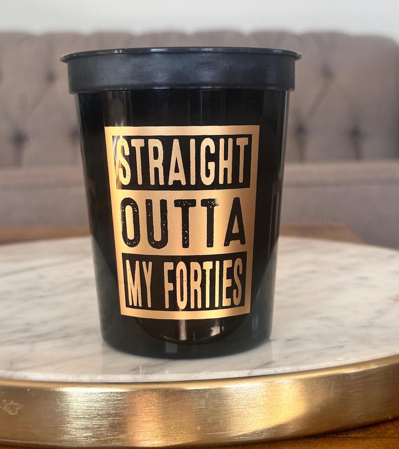 A single black cup featuring a gold box and text that reads Straight Outta My Forties rests on a marble tray.