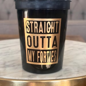Close-up of one black plastic party cup with gold metallic text reading Straight Outta My Forties.
