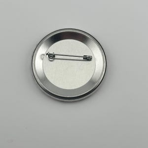 May include: The back of a silver button with a safety pin attached.