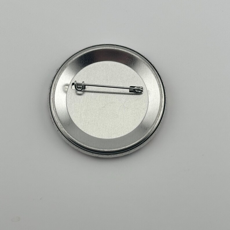 May include: The back of a silver button with a safety pin attached.