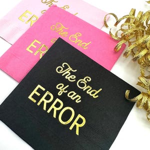 Three square paper napkins, one black, one pink, and one light pink, with "The End of an ERROR" in gold foil script on each, with gold ribbon.