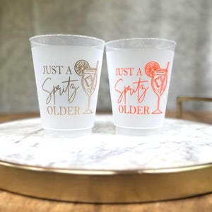16 ounce frosted cups that read Just a Spritz older, with an Aperol spritz image.  The font is in gold, and orange.  Plastic Birthday Cups for any age