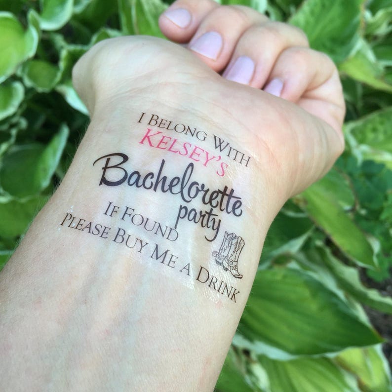 A temporary tattoo on a person's inner wrist reads "I BELONG WITH KELSEY'S Bachelorette party IF FOUND PLEASE BUY ME A DRINK" with two cowboy boots, against a green leafy background.