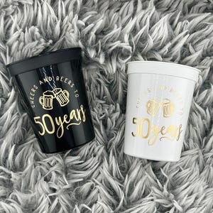 Black and White Plastic Stadium Cups that read cheers and beers to 50 years in gold text.  50th Milestone Cups