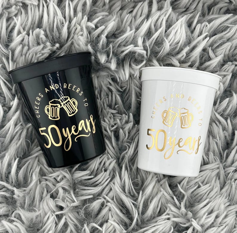 Black and White Plastic Stadium Cups that read cheers and beers to 50 years in gold text.  50th Milestone Cups