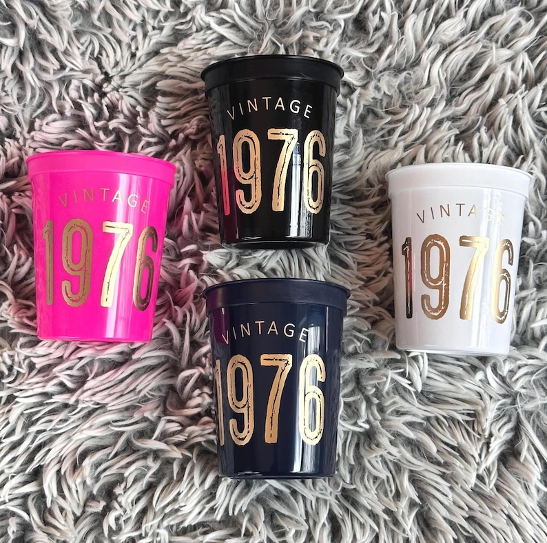 16 ounce stadium cups that read Vintage 1976 in gold metallic font.  the cups are black, navy, white and hot pink.  50th Birthday Cups